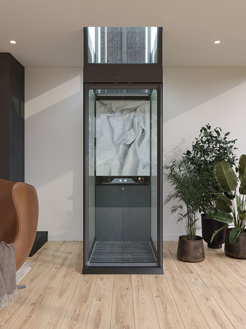 A living room showing an Aritco HomeLift Compact with full glass shaft installed against a wall showing how space efficient it is.